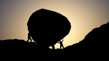 People helping each other move a boulder